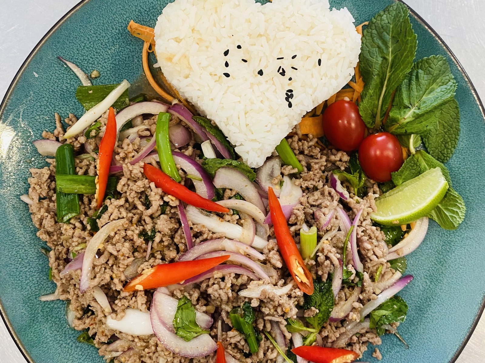 Laab mit Schweinefleisch, roten Zwiebeln, Chili und Kräutern, Reis in Herzform und Kirschtomaten