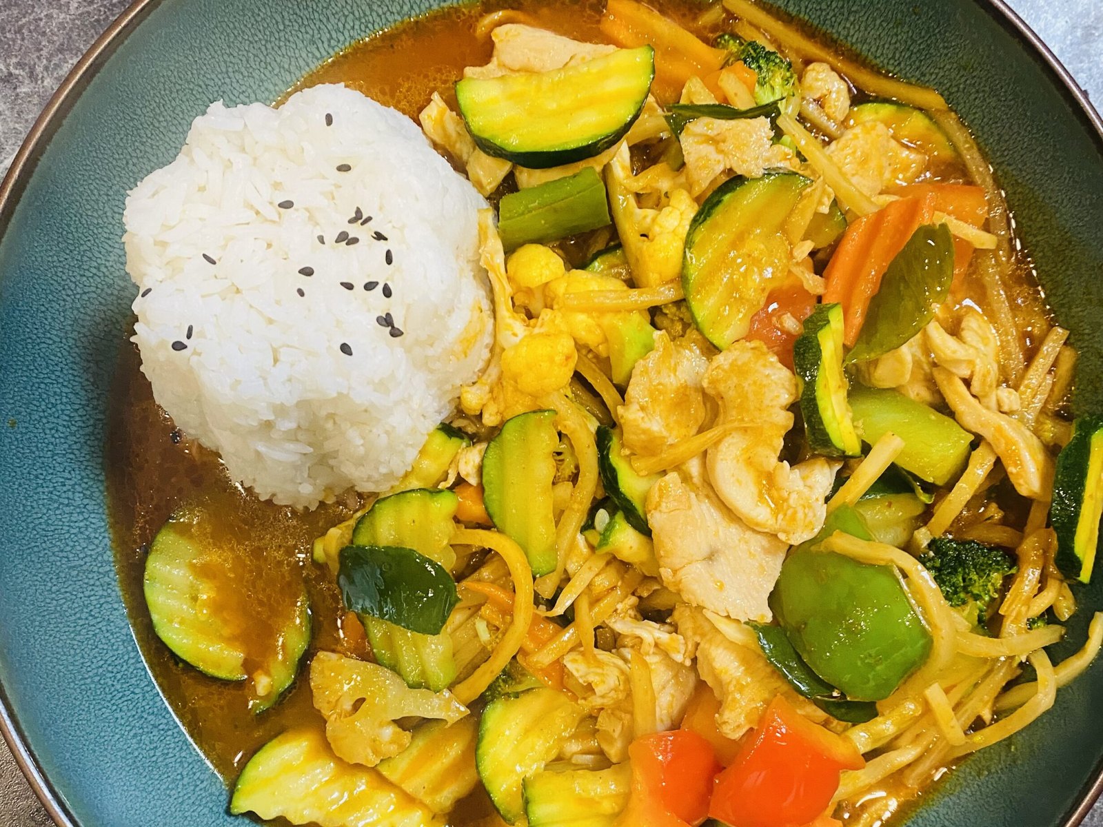 Gai Pad Prik Gaeng: Hühnerfleisch mit Gemüse in roter Currypaste, dazu ein Türmchen Reis, in einer türkisen Schale